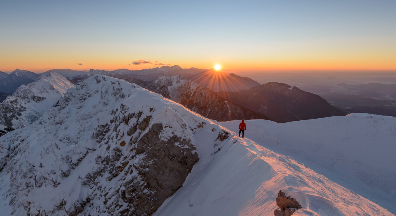 Black mountaineer silhouetted against sunrise on Himalayan peak with Everest visible in background
