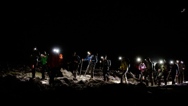 Corporate team celebrating summit success at night on Carrauntoohil with headtorches illuminating Irish mountain peak