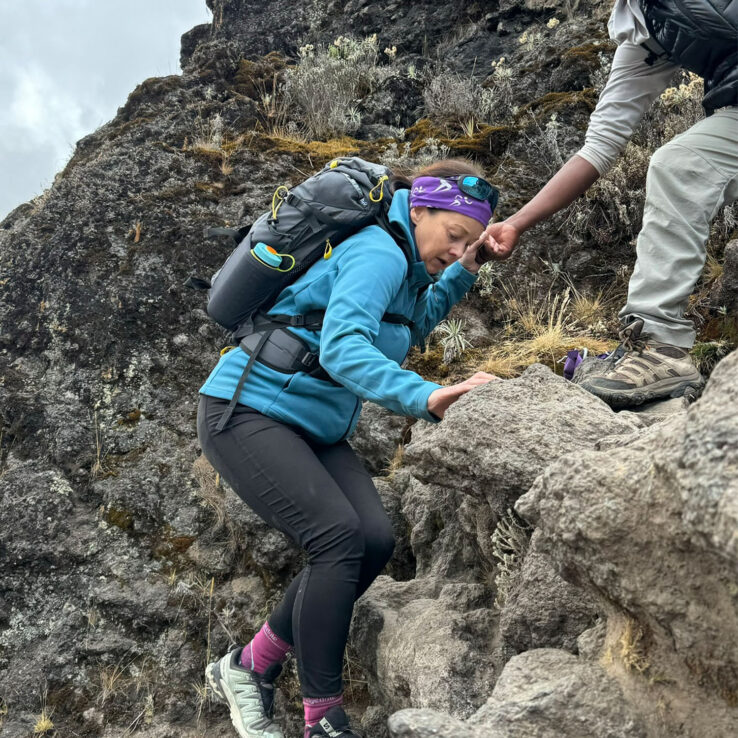 Business professionals supporting struggling colleague during mountain climb showing teamwork and collective care